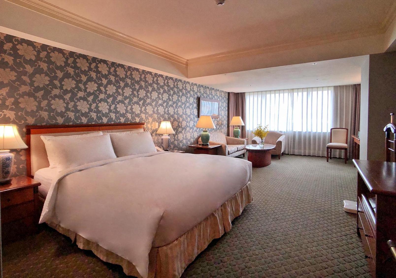 Evergreen Laurel Hotel - Taichung Exterior foto The photo shows a hotel room with a spacious and comfortable layout. It features a large bed with white bedding, placed against a decorative wallpapered wall. On either side of the bed, there are lamps providing soft lighting. In addition to the bed,