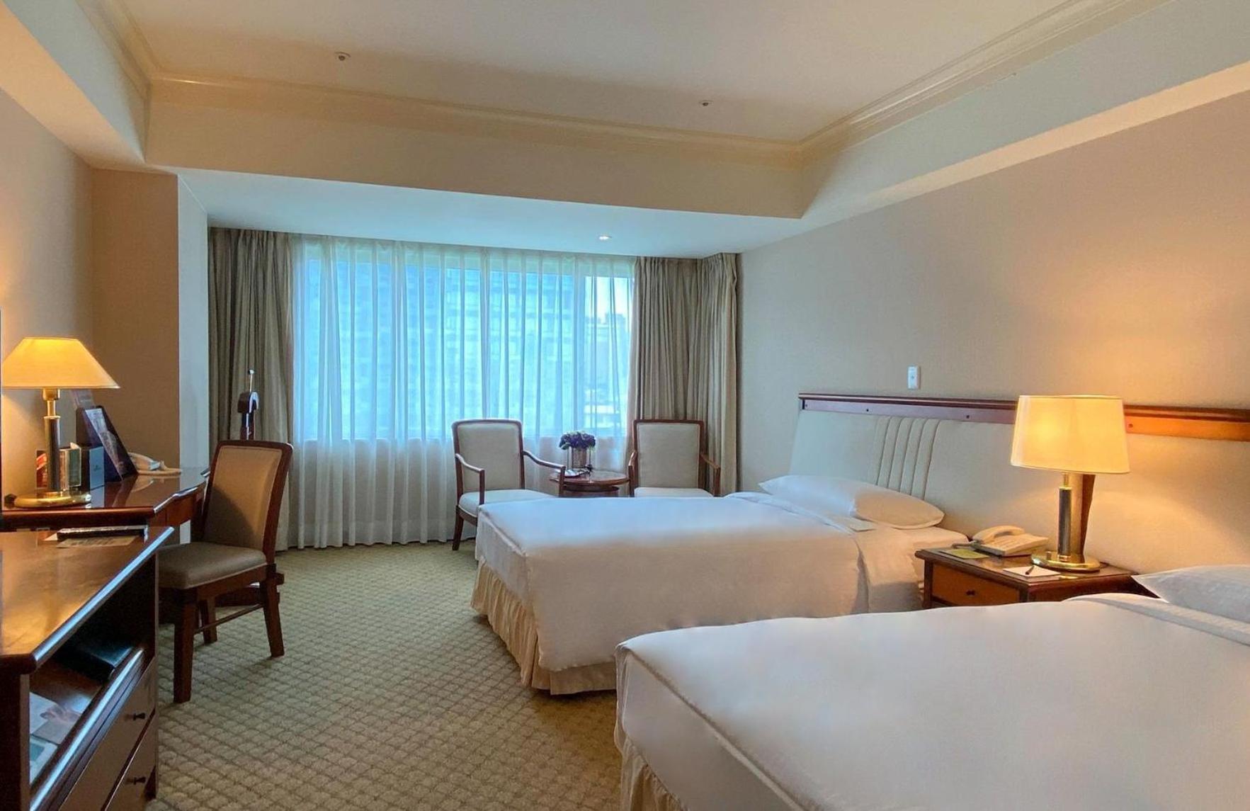 Evergreen Laurel Hotel - Taichung Exterior foto The photo shows a hotel room featuring two single beds positioned near each other. There's a light-colored carpet on the floor and a large window with sheer curtains that allows natural light to fill the space. In the room, there are two chairs place