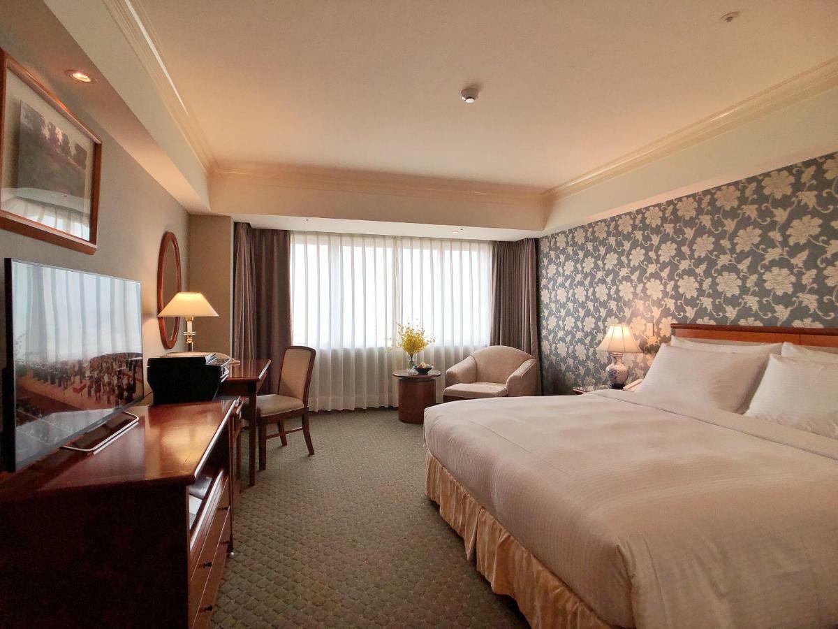 Evergreen Laurel Hotel - Taichung Exterior foto The photo shows a hotel room with a spacious layout. It features a large bed with white bedding, bedside lamps, and a decorative headboard. There is a comfortable seating area with an armchair and small table. A desk is present, complete with a lamp 