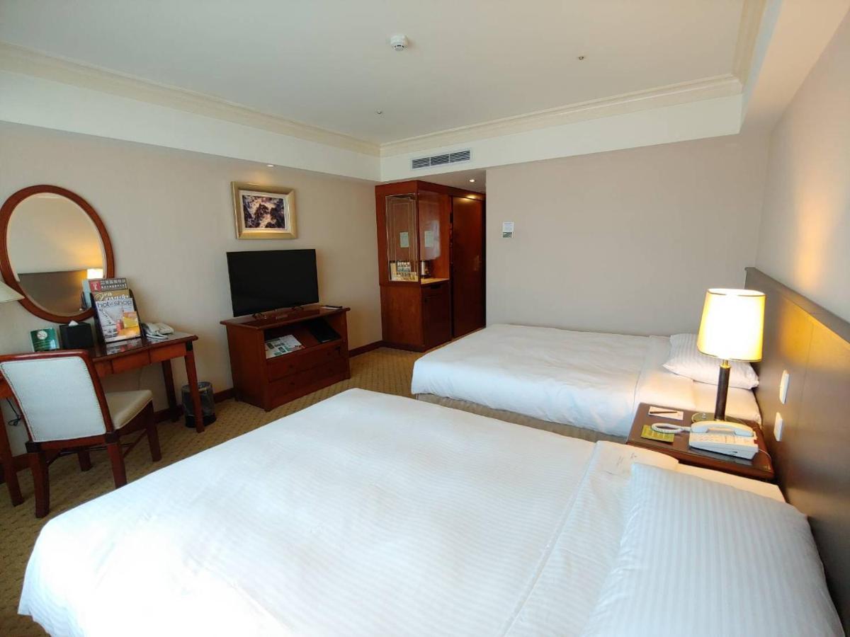 Evergreen Laurel Hotel - Taichung Exterior foto The photo shows a hotel room with two beds, neatly made with white linens. There is a desk and chair in one corner, accompanied by a flat-screen TV mounted on the wall. A large mirror and a wooden cabinet are also visible. The room is illuminated by 